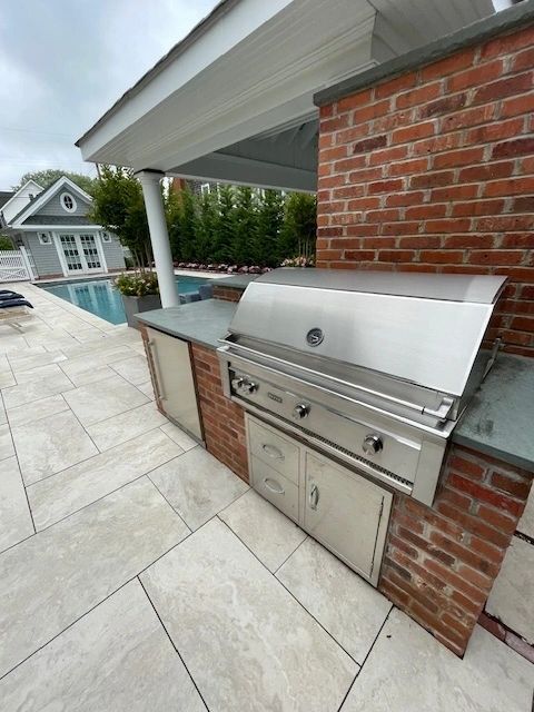Outdoor kitchen with built-in grill and pool in background